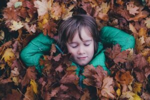 Child lying on a bed of autumn leaves